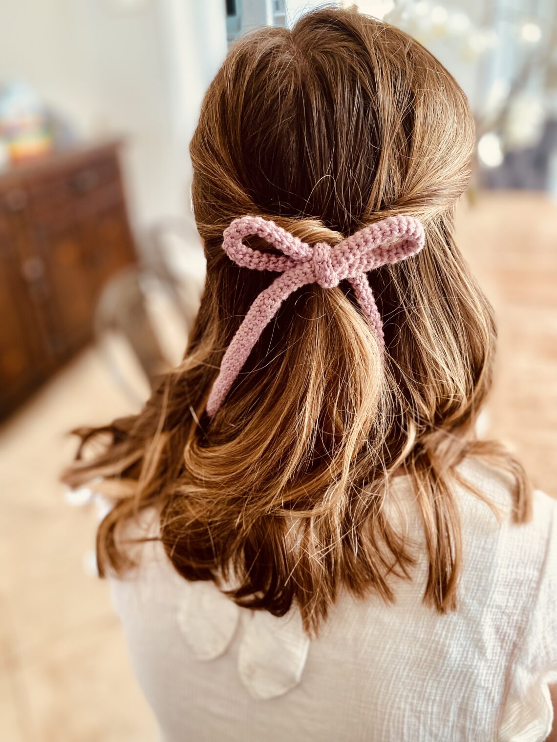 Picture of the back of a brown haired girls hair with a pink crocheted hair bow accessorizing her hair.