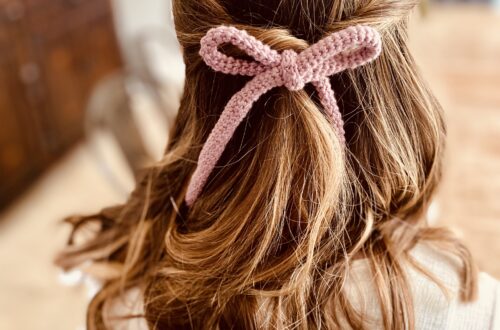 Picture of the back of a brown haired girls hair with a pink crocheted hair bow accessorizing her hair.