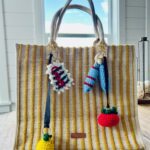 Striped Yellow and white bag decorated with Amalfi Coast inspired bag charms, sitting on a wooden table.