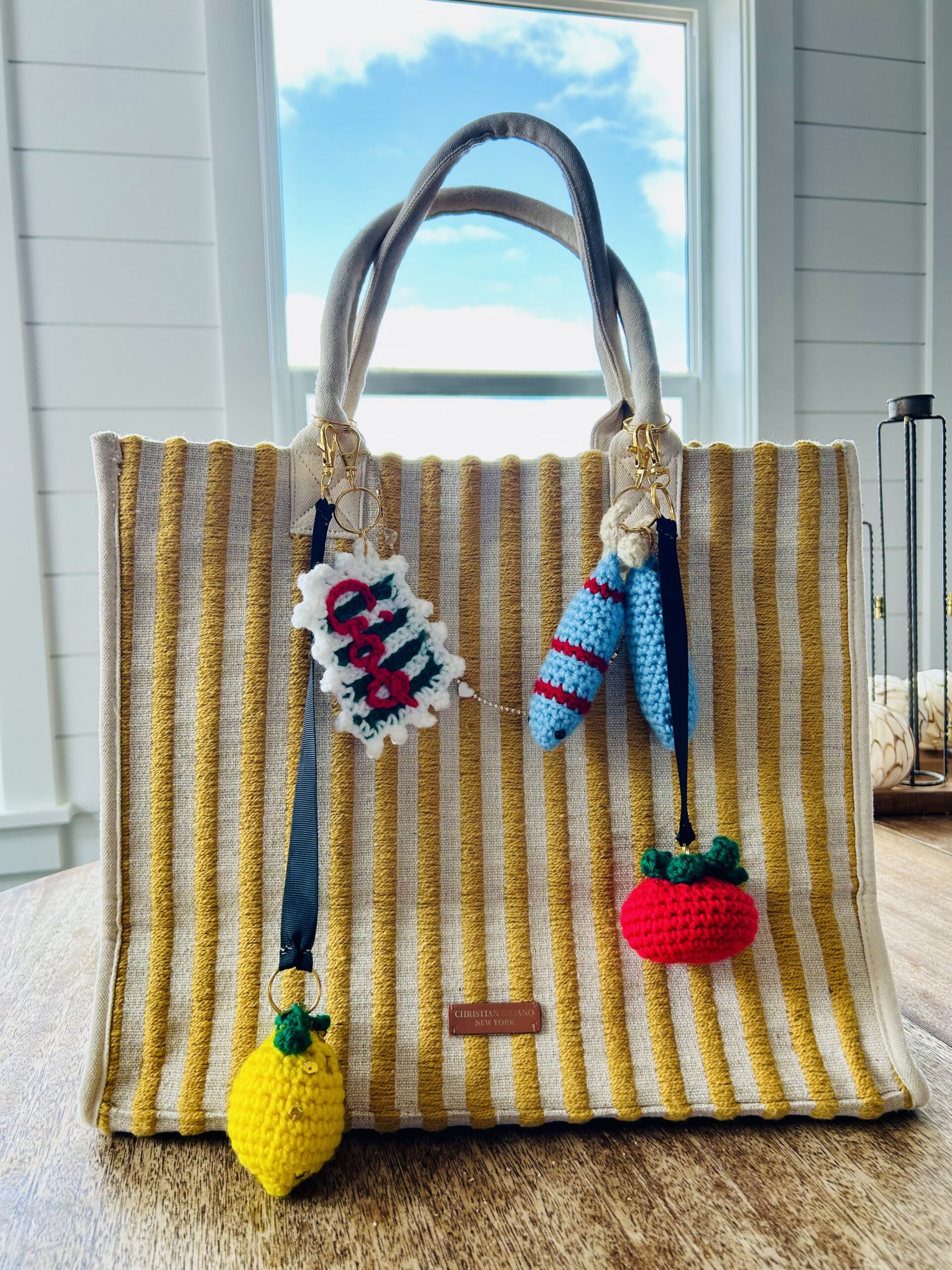 Striped Yellow and white bag decorated with Amalfi Coast inspired bag charms, sitting on a wooden table.