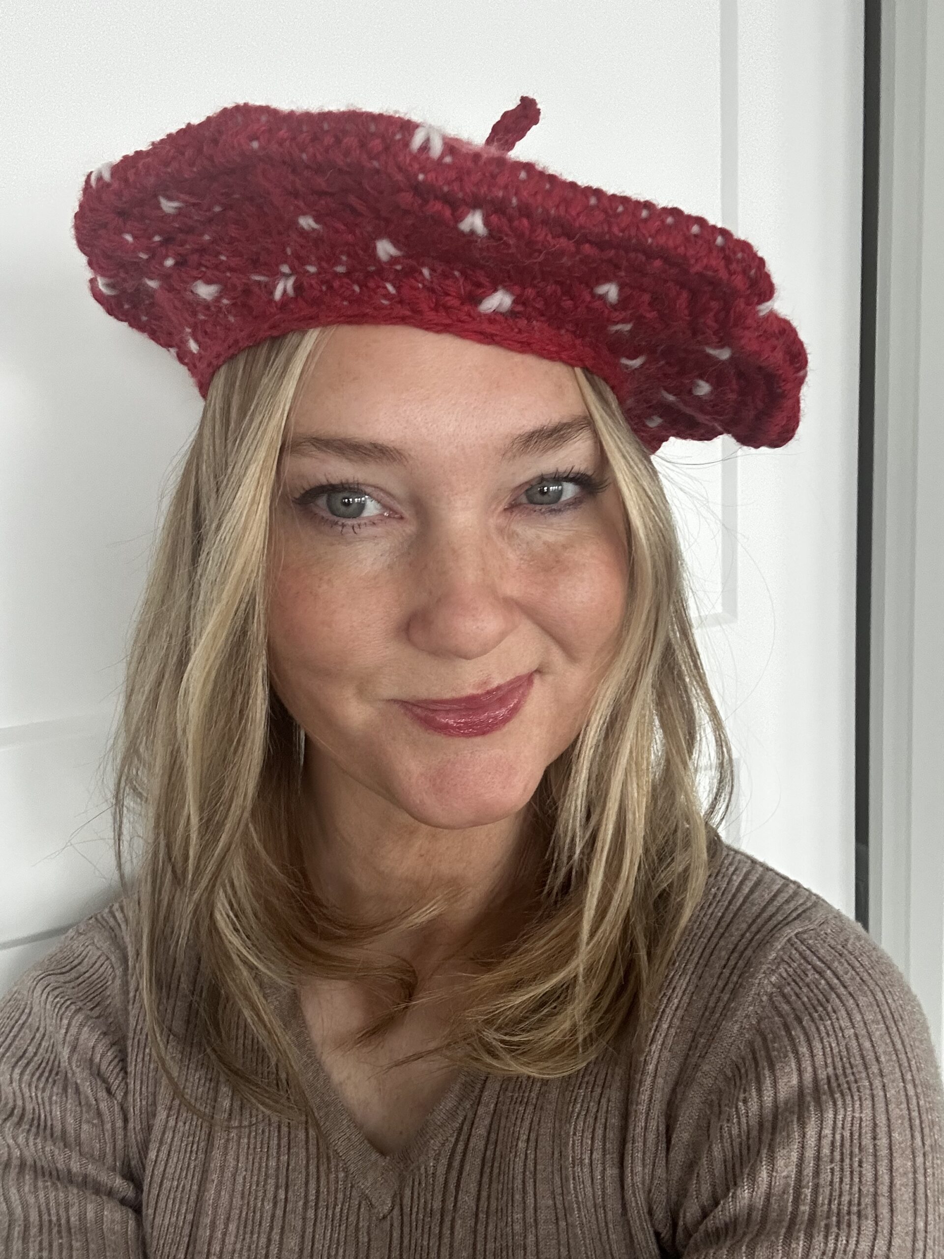 Blonde girl wearing the Be Mine Beret. A red crocheted beret with hearts.